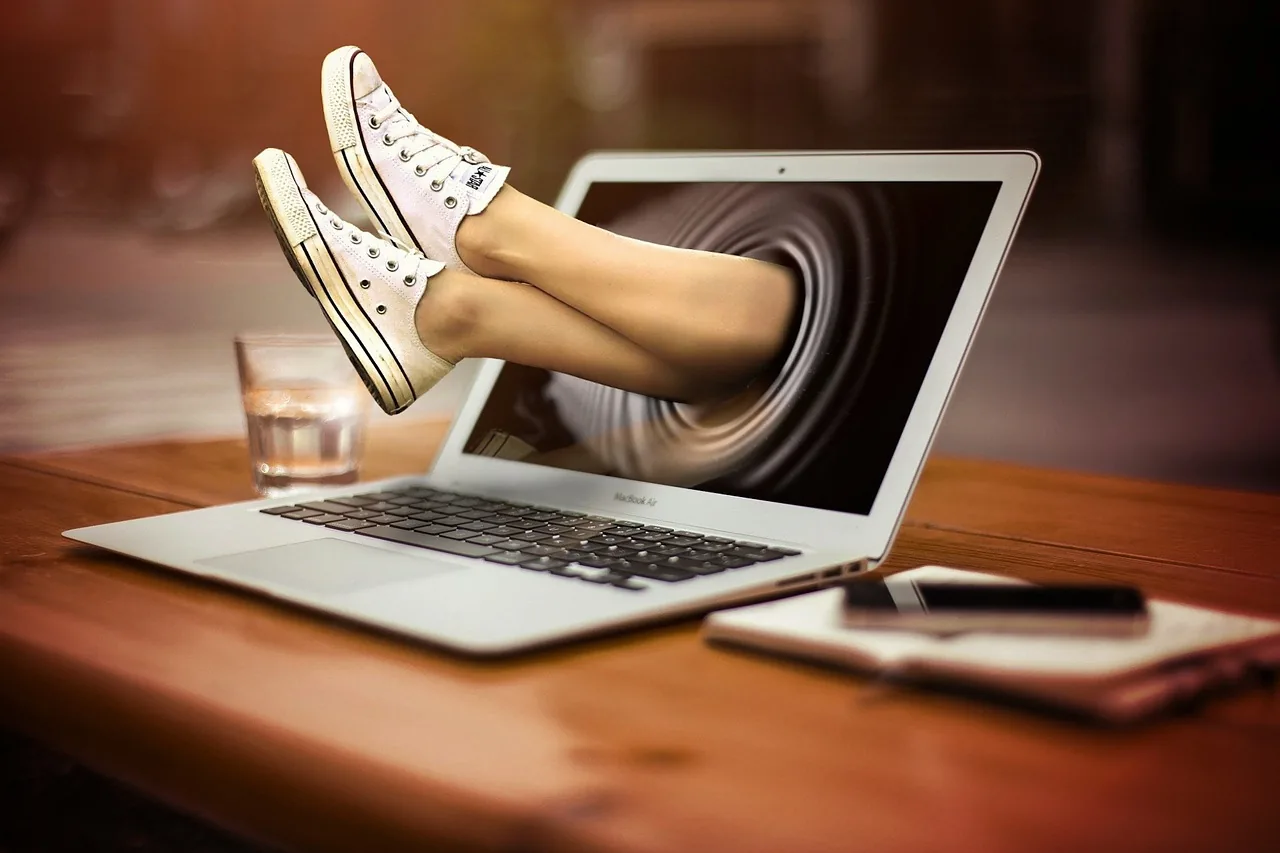 A pair of legs in sneakers kicking out through a laptop screen