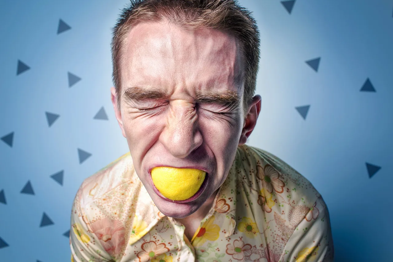 A man screwing up his face with a lemon wedge in his mouth