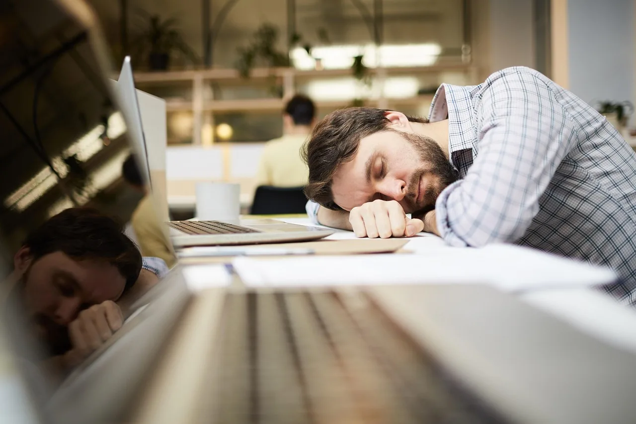 Two colleagues asleep at their desks in an open-plan office